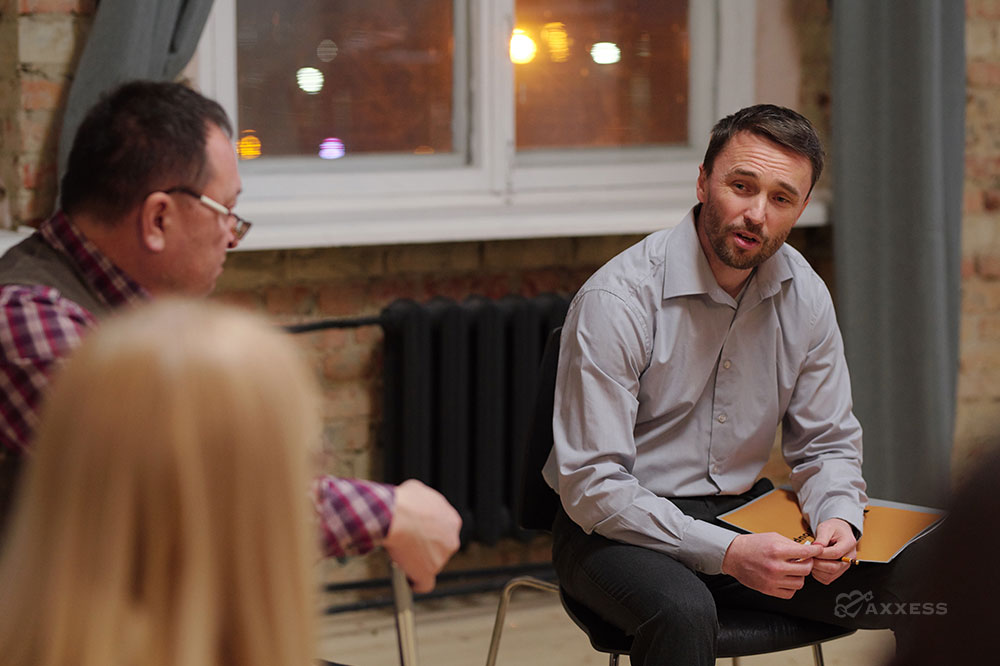 Middle-aged male counselor sits in a chair and leads a group conversation.