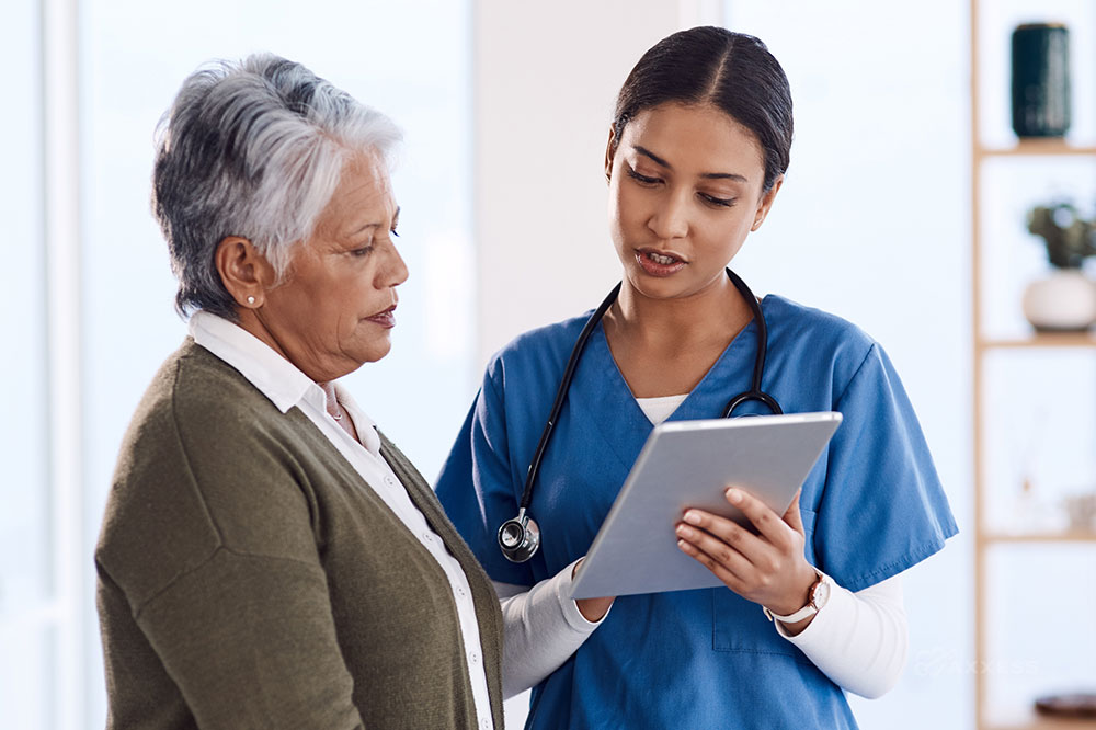 A female clinicians holds a tablet while speaking with an older female client.