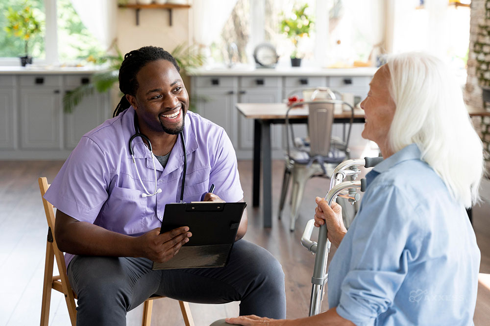Male clinician sits on a chair and smiles while speaking with an elderly female client