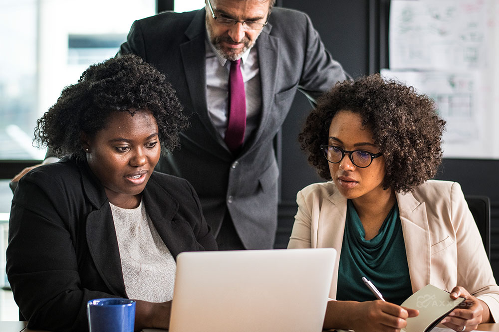 Three business people look at a laptop