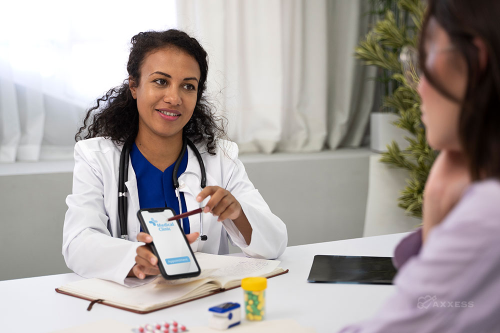 A female doctor sits at a table with a female patient and points to her phone screen