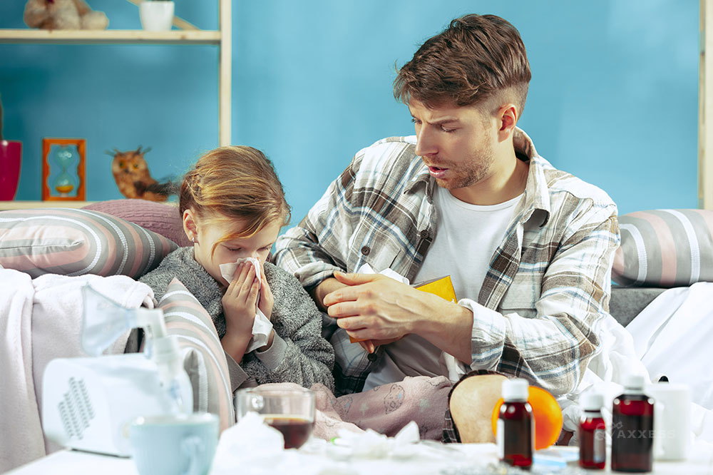 A father sits on a couch with a child blowing their nose
