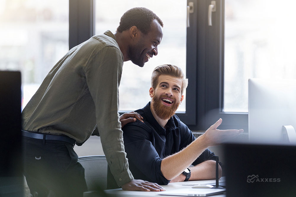 Two male business professionals smile while looking at a computer screen