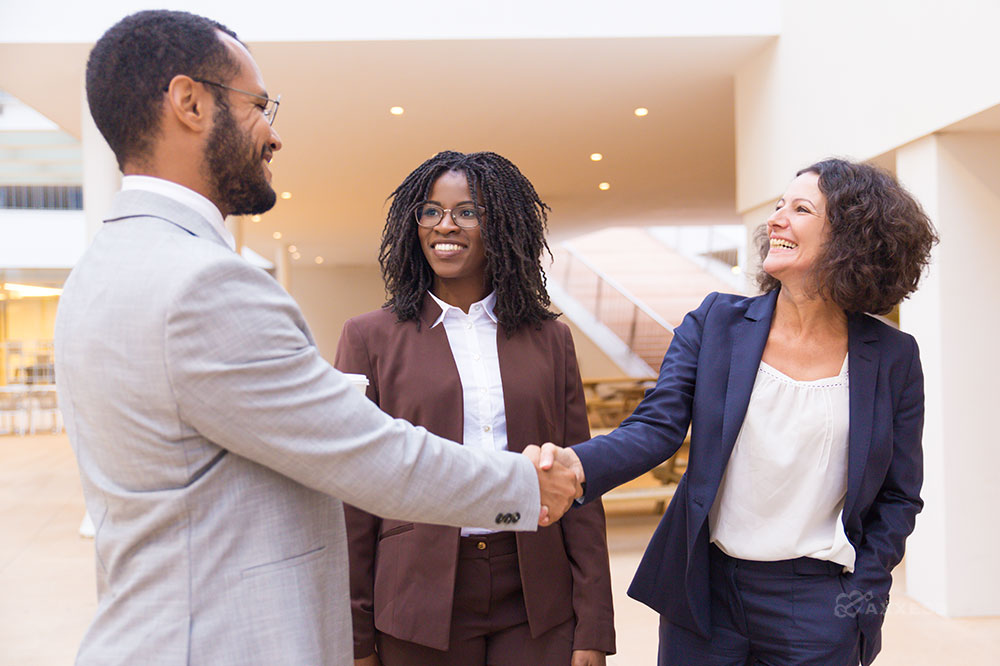 Three business professionals smile and shake hands.