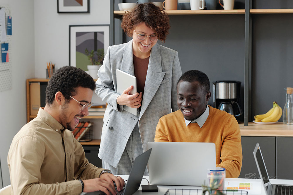 Three business professionals smile while looking at laptops