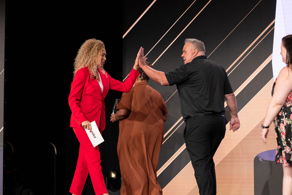A moment of celebration on the AGILE conference stage in Dallas as healthcare leaders exchange a high five while recognizing achievement and community in the home health and hospice industry.